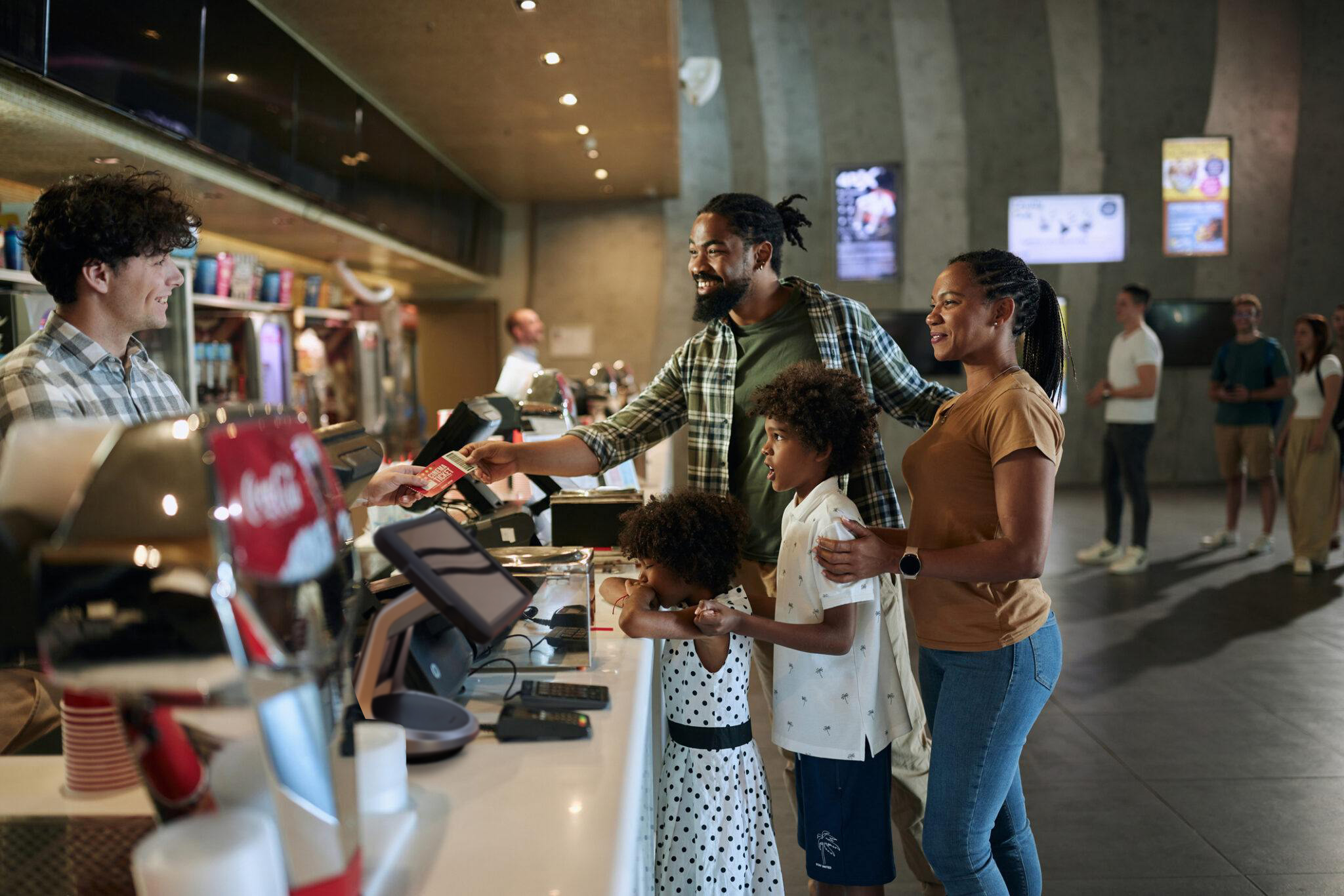 Glückliche afroamerikanische Eltern und ihre Kinder kaufen Eintrittskarten am Verkaufsstand in der Sportarena.