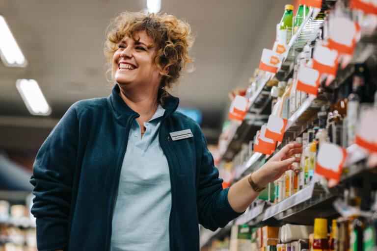 Selbstbewusste Geschäftsfrau, die an den Regalen steht und im Supermarkt lächelt. Weibliche Managerin in einem Lebensmittelladen.